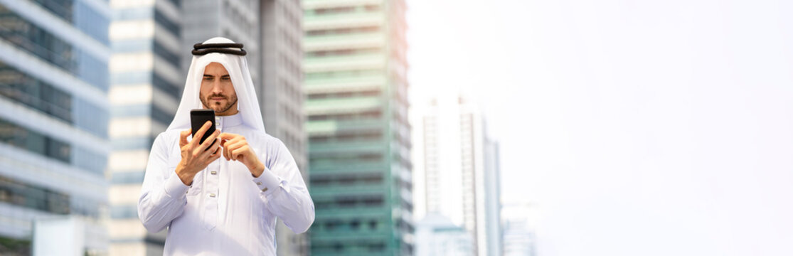 Contact us, A Business Caucasian Arab man using smartphone surfing on the internet or messaging, wearing traditional garment dishdasha and thobe, within city center nature  busy road for banner