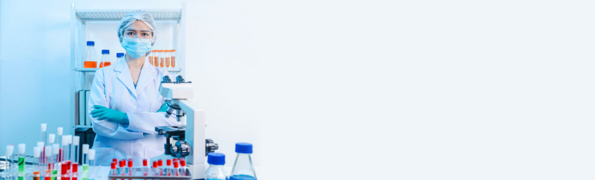 Asian people scientist in lab coat and protective gloves working with test tubes with green and red liquids, with microscope and other test tubes in the background in laboratory.