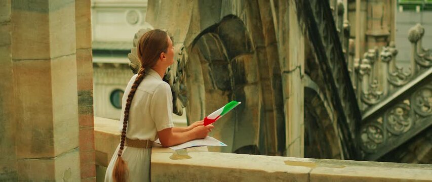 翻译标题：手持意大利国旗的女子俯瞰米兰大教堂建筑