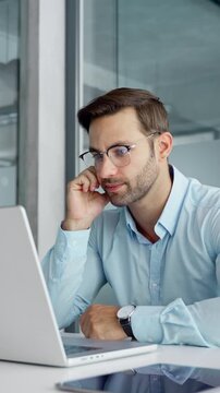 Confused young trader businessman looking disappointed at laptop pc computer screen having stress. Tired European business man holding hand near temples, feeling stressed sitting in office. Vertical