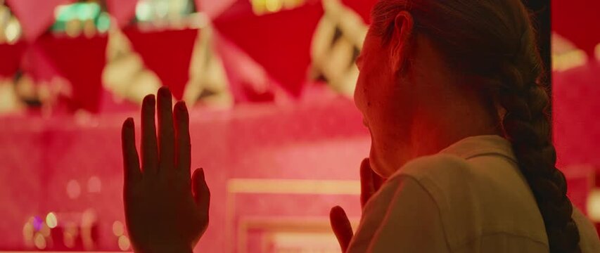 一位女士将手按在一家奢侈品牌店的玻璃墙上，在米兰夜晚漫步时，店内优雅的红金色内饰衬托下，她露出温暖的笑容。